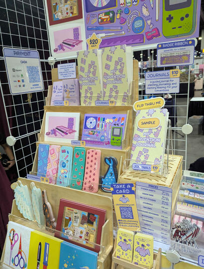 Table closeup May 2026 - zines, journals, prints, bookmarks, ribbons